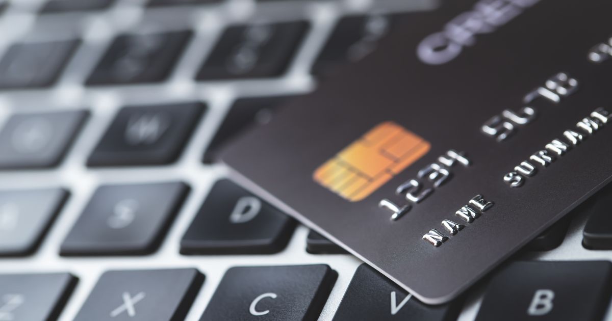 Grande plano de um cartão preto com chip dourado e números em relevo, pousado sobre o teclado de um portátil